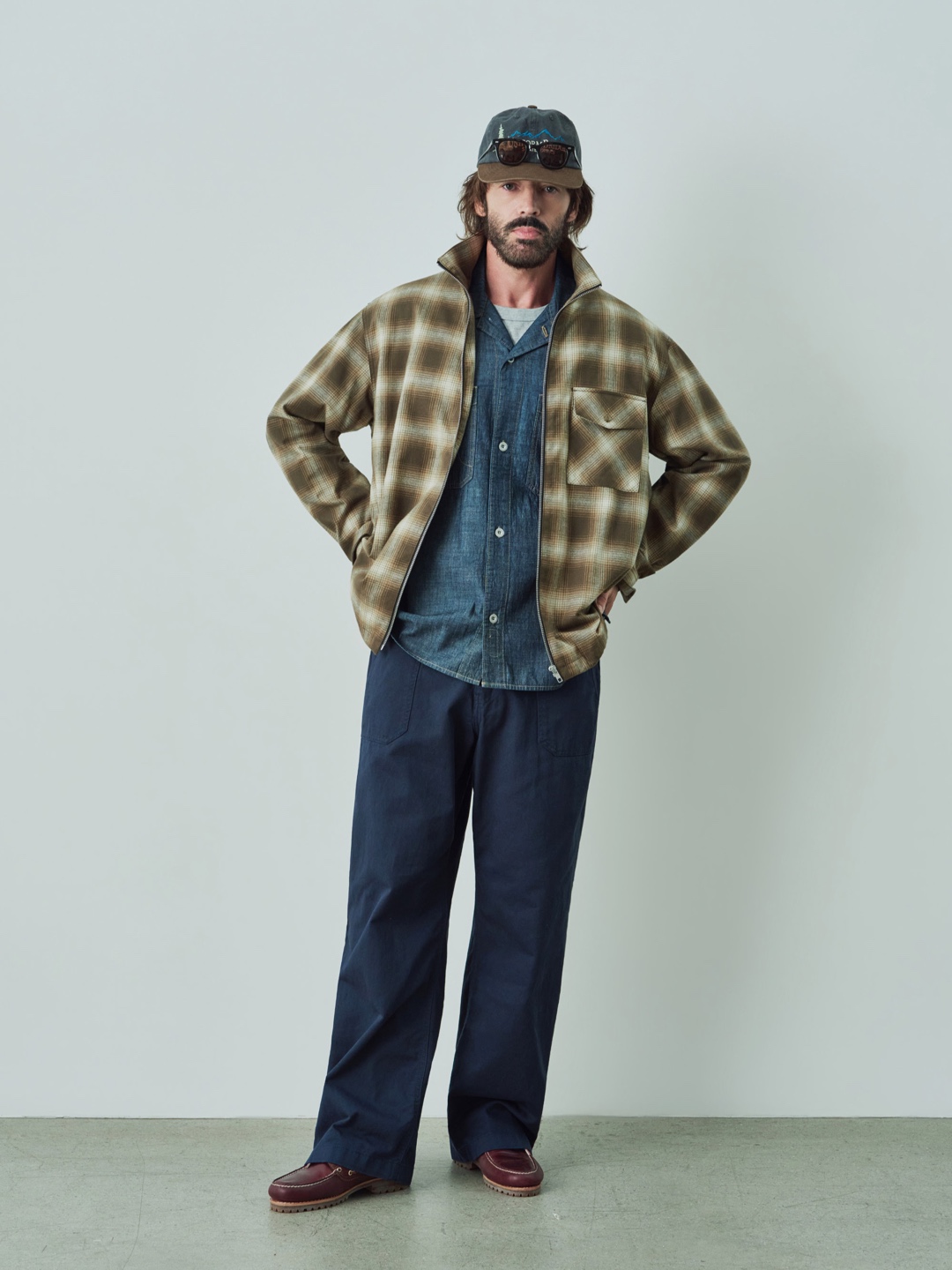 棕色格纹 overshirt 里面只露出蓝色内层，深蓝裤子把颜色压住。